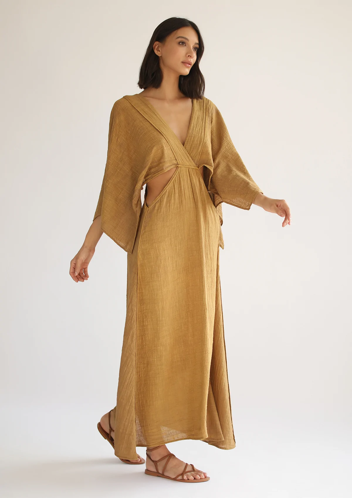Woman wearing a flowing golden brown maxi dress with cape sleeves and waist cutouts